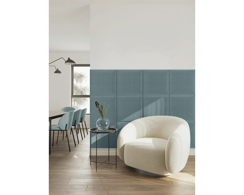 Modernes, helles Wohnzimmer mit blauen gepolsterten Wandpaneelen aus Textil hinter einem weißen Sessel.