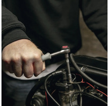 Hand bedient eine kleine Umschaltknarre mit grauem Griff an einem Motorteil.