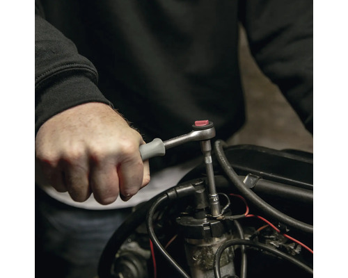 Hand bedient eine kleine Umschaltknarre mit grauem Griff an einem Motorteil.
