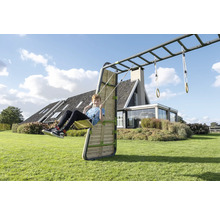Kind auf einer Schaukel an einem Klettergerüst mit Hangelstangen und Holzwand in einem hellen, geräumigen Garten vor einem Wohnhaus.