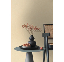 Beige Vliestapete mit feiner Textur in einem minimalistischen Raum mit Beistelltisch, schwarzer Vase und Rattan-Stuhl.