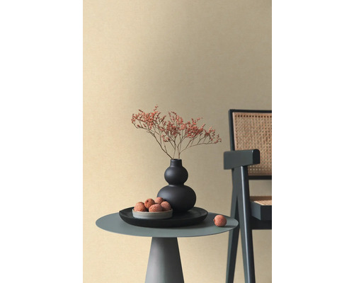 Beige Vliestapete mit feiner Textur in einem minimalistischen Raum mit Beistelltisch, schwarzer Vase und Rattan-Stuhl.
