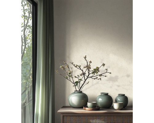 Helles Wohnzimmer mit hölzernem Sideboard, darauf grüne Keramikvasen mit Zweigen vor einer Wand mit strukturierter Farbe und Vorhängen.