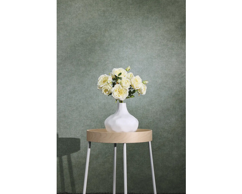 Grüne strukturierte Vliestapete mit Textiloptik hinter einem Beistelltisch mit Blumenvase.