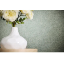Einfarbige Vliestapete mit feiner Leinenstruktur in einem hellen Grünton hinter einer weißen Vase mit Blumen.