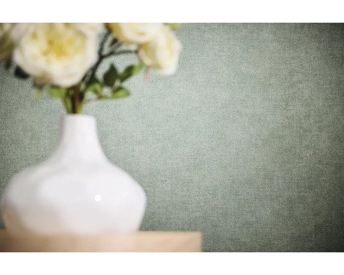 Einfarbige Vliestapete mit feiner Leinenstruktur in einem hellen Grünton hinter einer weißen Vase mit Blumen.
