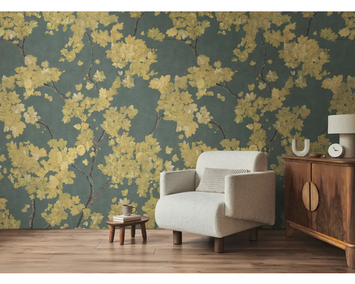Vlies-Fototapete mit gelben Blütenzweigen auf dunklem Hintergrund im Wohnzimmer mit hellem Sessel und Holzmöbeln auf Laminatboden.