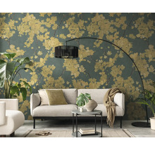 Wohnzimmer mit Vliestapete im floralen Muster, gelbe Blüten auf dunkelgrünem Hintergrund, hellgraues Sofa und schwarze Bogenlampe.