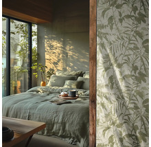 Schlafzimmer mit hellgrüner Leinenbettwäsche und Tapete mit botanischem Blattmuster vor einem sonnigen Fenster.