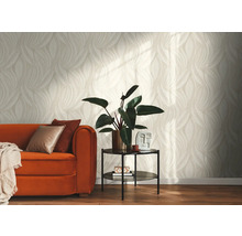 Helles Wohnzimmer mit Tapete in beige-weißem Blättermuster, einem orangefarbenen Sofa mit Kissen und einem Beistelltisch mit Zimmerpflanze.