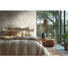 Hell gestaltetes Schlafzimmer mit Tapete im Blattdesign, einem Bett mit Leinenbezug, großem Fenster und natürlichen Dekoelementen.