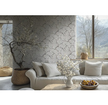 Vliestapete mit feinem Zweig- und Blütenmuster an einer Wand in einem hellen Wohnzimmer hinter einem Sofa mit Kissen.