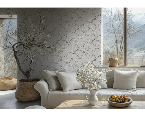 Vliestapete mit feinem Zweig- und Blütenmuster an einer Wand in einem hellen Wohnzimmer hinter einem Sofa mit Kissen.
