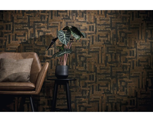 Wandgestaltung mit geometrisch gemusterter Tapete in Braun und Schwarz, brauner Ledersessel mit Kissen und eine Zimmerpflanze auf einem Beistelltisch.