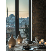 Gedeckter Esstisch mit Kerzen, Gläsern und Vasen vor einem Fenster mit Stadtblick und geometrisch gemusterter Tapete.
