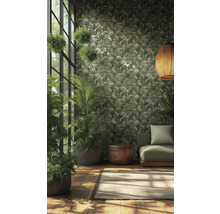 Vliestapete mit tropischem Blattmuster in Grün und Creme in einem hellen Raum mit Zimmerpflanzen, grünem Sofa und geflochtener Hängelampe.