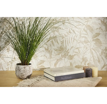 Vliestapete mit botanischem Blattmuster in hellen Tönen, kombiniert mit einer Zimmerpflanze, Büchern und Kerzen auf einem Holztisch.