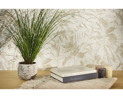Vliestapete mit botanischem Blattmuster in hellen Tönen, kombiniert mit einer Zimmerpflanze, Büchern und Kerzen auf einem Holztisch.