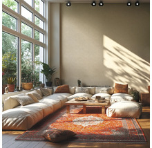 Helles Wohnzimmer mit großem Ecksofa, Holztisch und buntem Orientteppich vor einer hohen Fensterfront mit Blick ins Grüne.