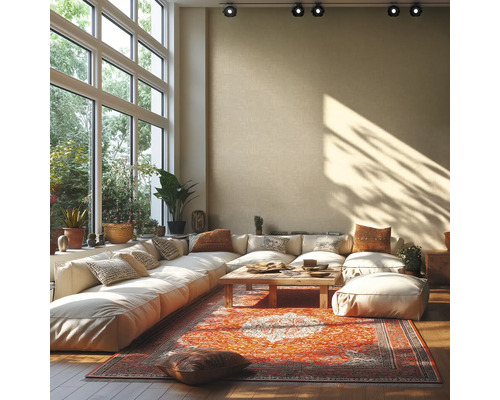 Helles Wohnzimmer mit großem Ecksofa, Holztisch und buntem Orientteppich vor einer hohen Fensterfront mit Blick ins Grüne.