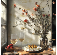 Rustikaler Tisch am Fenster mit Weißwein, Oliven, Fetakäse, Tomaten und einer Vase mit Trockenblumen vor einer texturierten Wand.