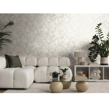 Helles Wohnzimmer mit Vliestapete im Blätterdesign, Modulsofa, Glastisch und verschiedenen Zimmerpflanzen.