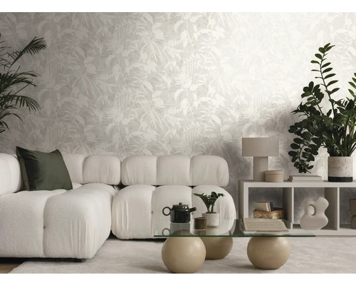 Helles Wohnzimmer mit Vliestapete im Blätterdesign, Modulsofa, Glastisch und verschiedenen Zimmerpflanzen.