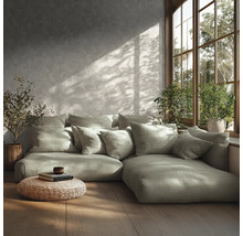 Modernes Wohnzimmer mit Modulsofa, vielen Kissen, gemusterter Tapete, Holzfußboden, geflochtenem Pouf und Pflanzen am sonnigen Fenster.