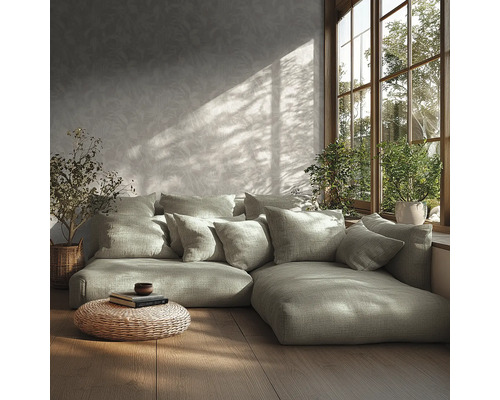 Modernes Wohnzimmer mit Modulsofa, vielen Kissen, gemusterter Tapete, Holzfußboden, geflochtenem Pouf und Pflanzen am sonnigen Fenster.