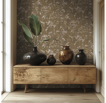 Hölzernes Sideboard vor einer Wand mit Tapete mit Blättermuster, dekoriert mit verschiedenen dunklen Vasen und großen grünen Blättern.