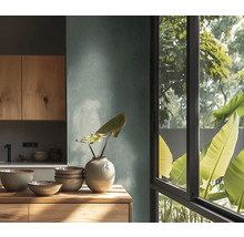 Moderne Küche mit strukturierter Wand, Holzschränken und Arbeitsplatte. Darauf Keramikschalen und eine Vase. Großes Fenster mit Blick auf Pflanzen.