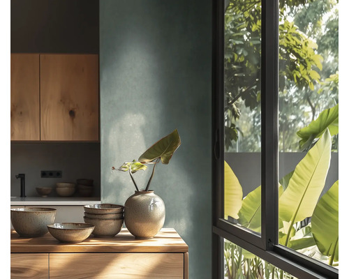 Moderne Küche mit strukturierter Wand, Holzschränken und Arbeitsplatte. Darauf Keramikschalen und eine Vase. Großes Fenster mit Blick auf Pflanzen.