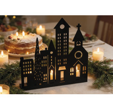 Schwarze Silhouette einer Winterstadt als Kerzenhalter auf einem festlich geschmückten Tisch mit Tannenzweigen und Kerzen.