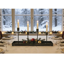 Adventskerzenhalter aus schwarzem Metall mit vier brennenden Kerzen, Tannenzweigen und Weihnachtskugeln auf einem festlich gedeckten Tisch.