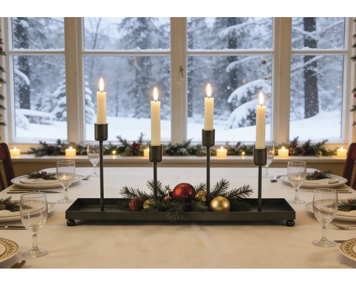 Adventskerzenhalter aus schwarzem Metall mit vier brennenden Kerzen, Tannenzweigen und Weihnachtskugeln auf einem festlich gedeckten Tisch.