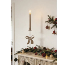 Schlanker Metallkerzenständer mit Schleife und brennender Kerze auf einer Kommode mit Weihnachtsdekoration aus Tannenzweigen und Kugeln.