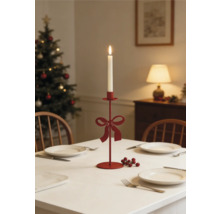 Roter Metall-Kerzenständer mit Schleife auf festlich gedecktem Weihnachtstisch mit brennender weißer Kerze und Weihnachtsbaum im Hintergrund.