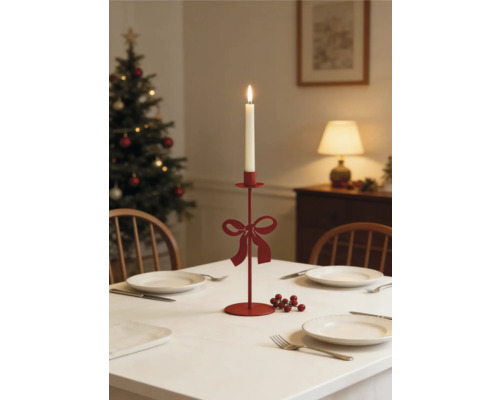 Roter Metall-Kerzenständer mit Schleife auf festlich gedecktem Weihnachtstisch mit brennender weißer Kerze und Weihnachtsbaum im Hintergrund.