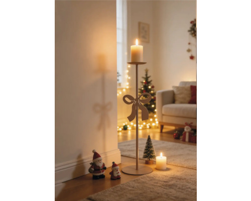 Hoher Metallkerzenständer mit dekorativer Schleife und brennender Kerze in einem weihnachtlich dekorierten Wohnzimmer mit Weihnachtsbaum und Figuren.