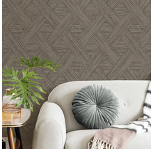 Tapete mit braunem geometrischem Muster hinter einem grauen Sofa mit rundem Samtkissen und einer Zimmerpflanze.