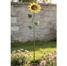 Gartenstecker Sonnenblume aus Metall in einem Blumenbeet mit rosa Blumen vor einer Steinmauer.