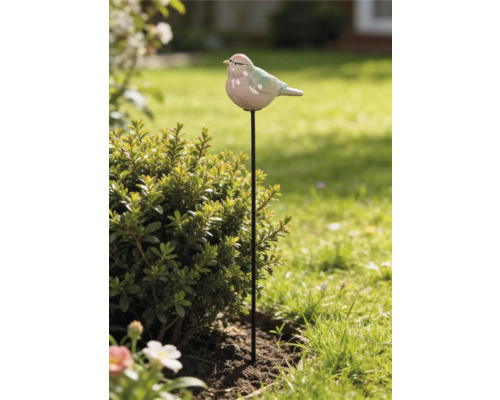 Gartenstecker mit Keramikvogel auf schwarzem Metallstab neben einem Strauch im Garten.