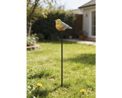 Gartenstecker mit einer kleinen Vogelfigur auf einem langen Metallstab, platziert in einer Rasenfläche vor einem Gartenhintergrund.
