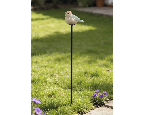 Gartenstecker aus Metall mit einer Vogelfigur aus Keramik in einem hellen Garten mit Rasen und Blumen.