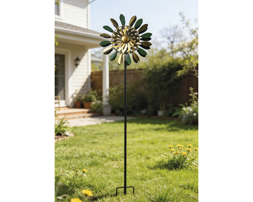 Kinetisches Windspiel aus Metall in Grün und Gold mit blattförmigen Elementen auf einem hohen Stab in einem sonnigen Garten auf dem Rasen.