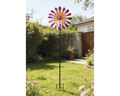 Buntes Windrad aus Metall auf einem schwarzen Stab, platziert in einem hellen Garten auf einer Rasenfläche.