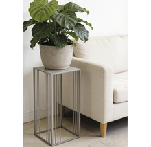 Moderner grauer Pflanzenständer aus Metall mit minimalistischem Design, darauf eine grüne Pflanze im Topf neben einem hellen Sofa im Wohnzimmer.