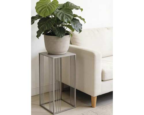 Moderner grauer Pflanzenständer aus Metall mit minimalistischem Design, darauf eine grüne Pflanze im Topf neben einem hellen Sofa im Wohnzimmer.