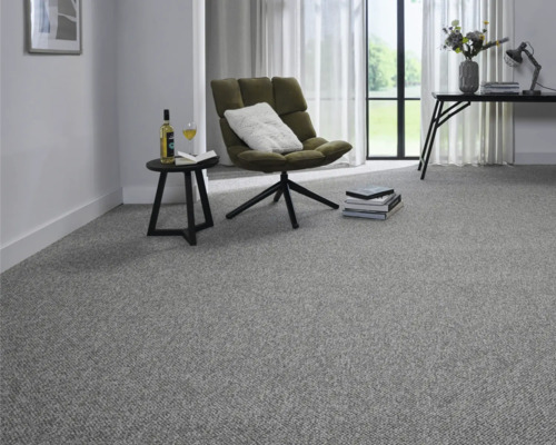 Hell gestaltetes, modernes Zimmer mit grauem Teppichboden, grünem Sessel, schwarzem Beistelltisch und großen Fenstern.
