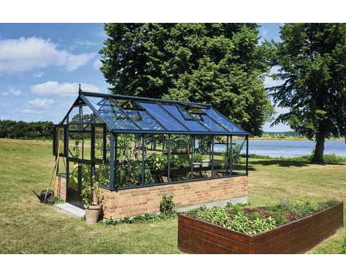 Großes Gewächshaus aus Glas und Metall auf einem Backsteinsockel mit geöffneten Dachfenstern in einem weitläufigen Garten am See.